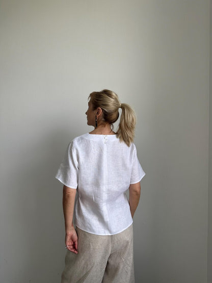 Woman wearing a white top and beige pants against a plain wall