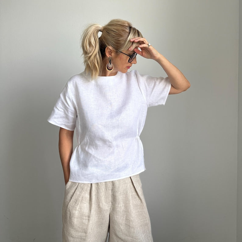 Woman wearing a white t-shirt and beige pants against a plain background