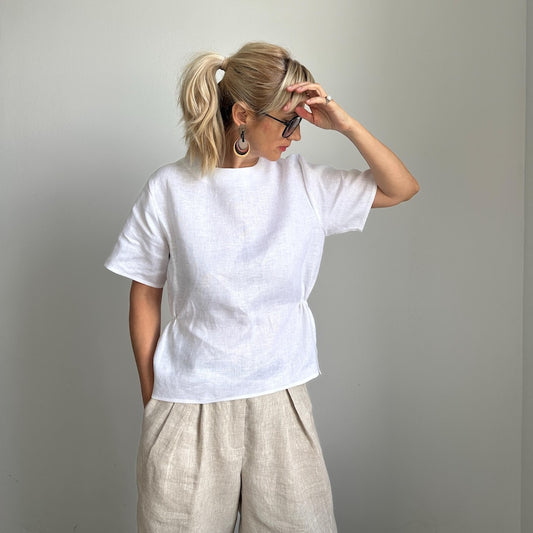 Woman wearing a white t-shirt and beige pants against a plain background