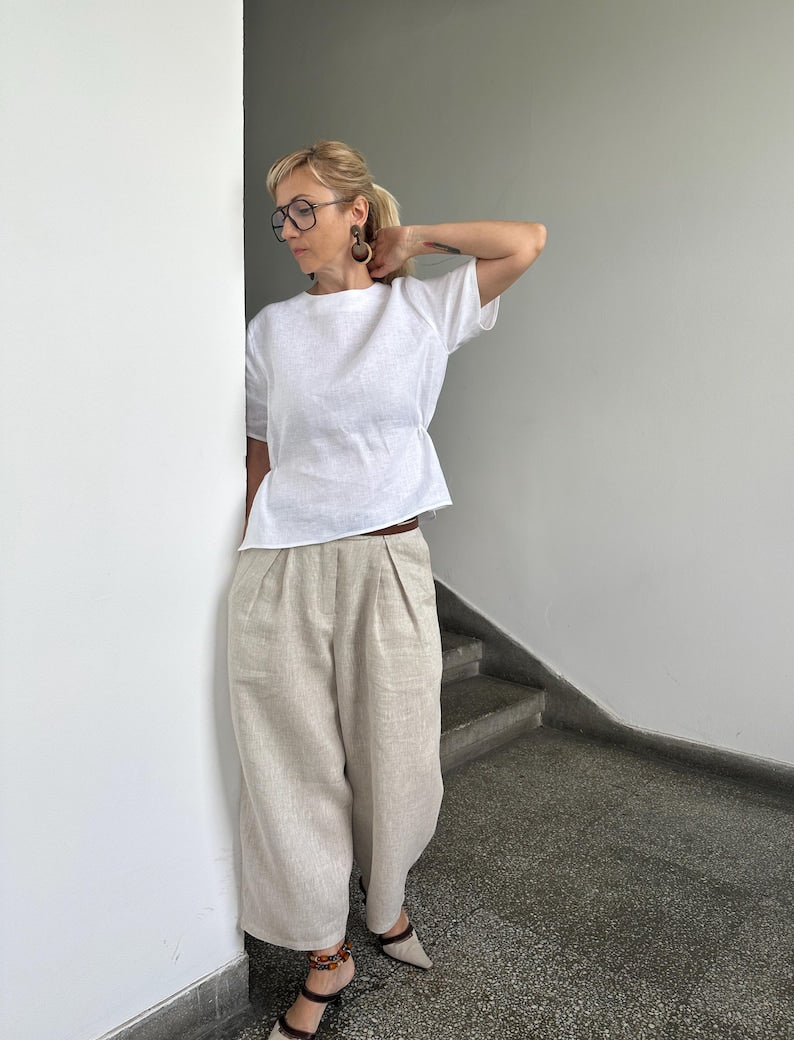 Person wearing a white top and beige pants against a plain wall.