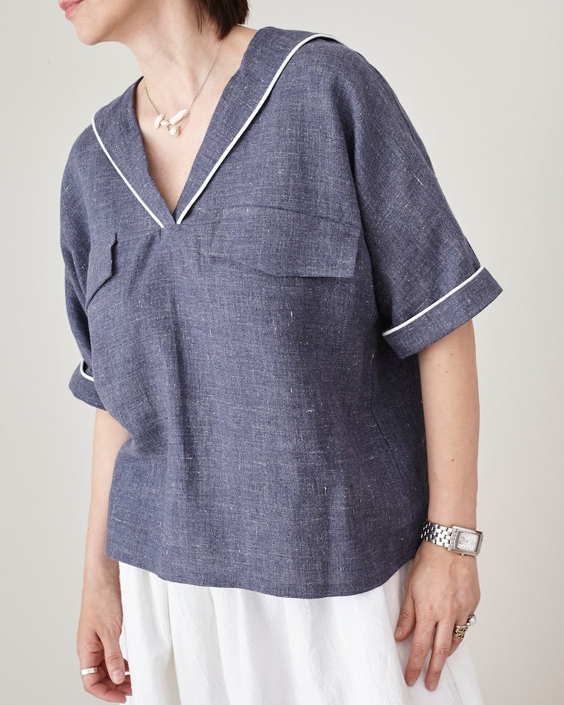 Person wearing a blue denim blouse with white piping on a plain background