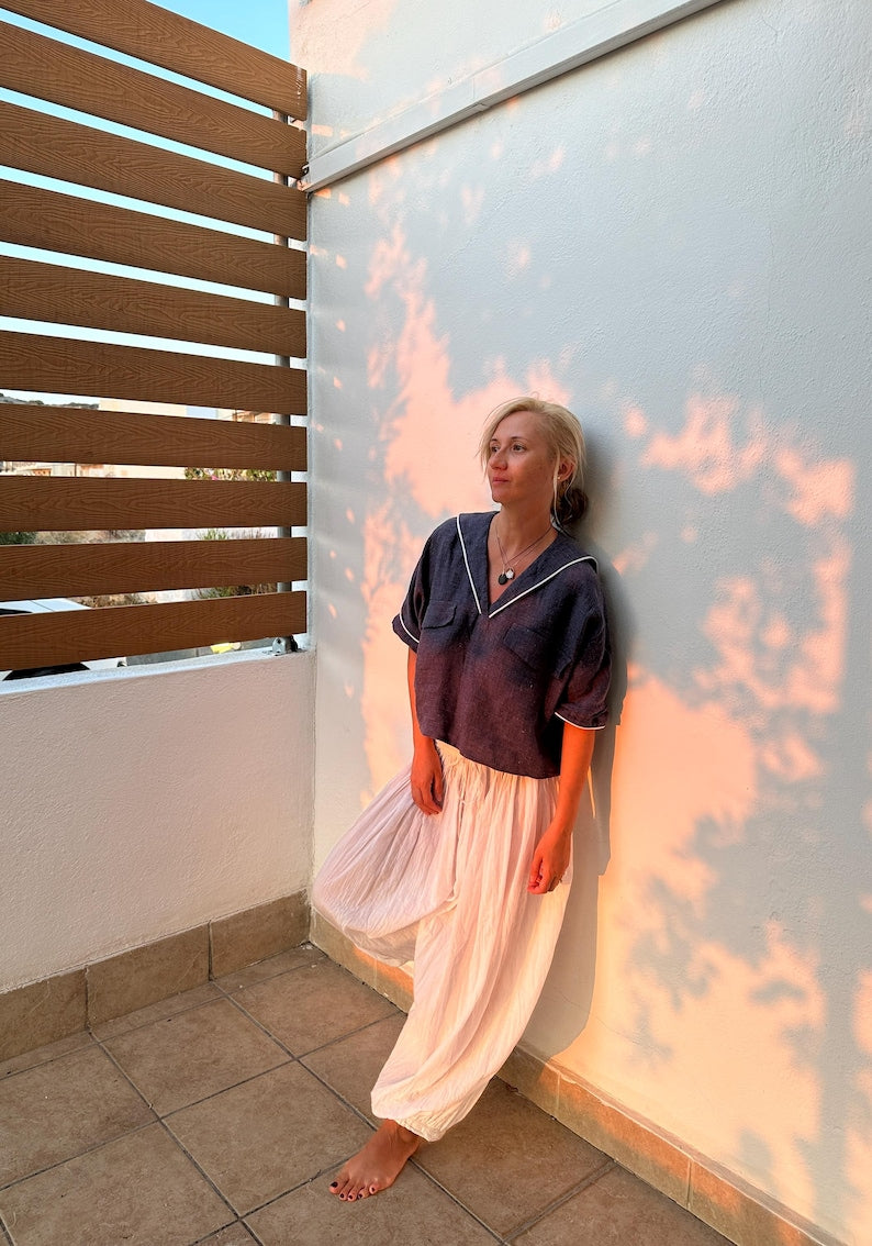 Woman leaning against a wall with a textured surface, wearing a blue sailor colllar top and white balloon pants
