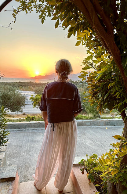 Person standing by a pool at sunset with scenic view wearing a sailor collar blue blouse and sheer balloon pants