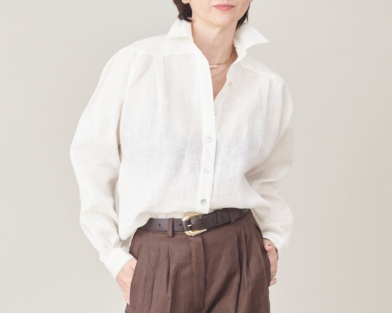 Person wearing a white shirt and brown pants against a plain background