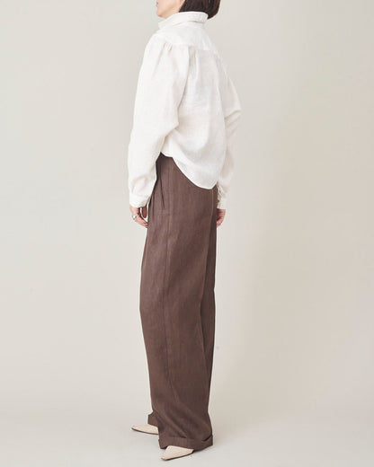 Person wearing a white shirt and brown pants on a plain background