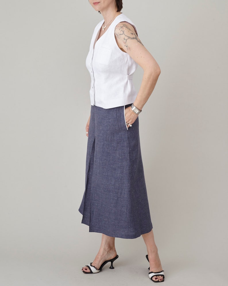 Woman wearing a white sleeveless top and blue denim skirt on a plain background