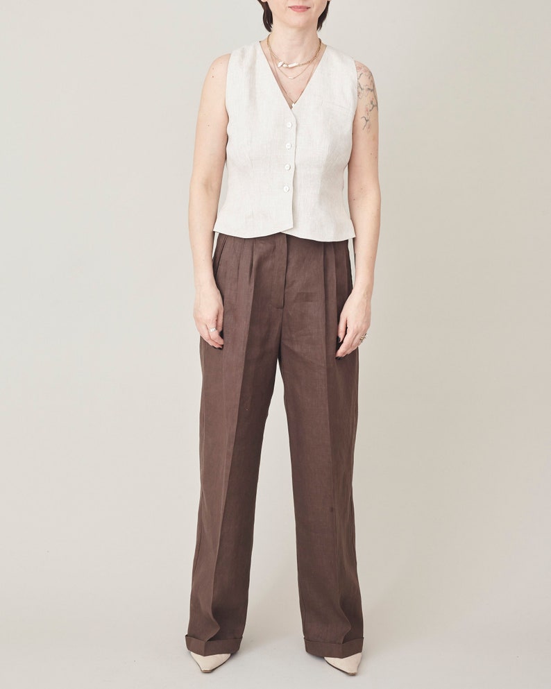 Person wearing a beige vest and brown pants on a plain background