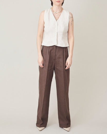 Person wearing a beige vest and brown pants on a plain background