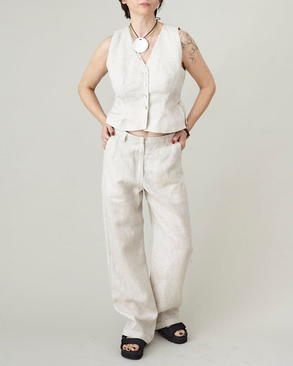 Person wearing a beige vest and matching beige pants against a plain background