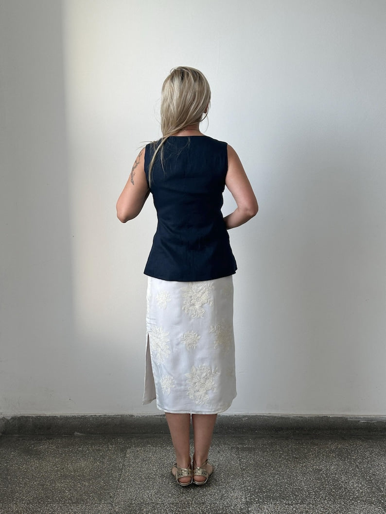 Woman wearing a navy top and white skirt with floral patterns against a plain background