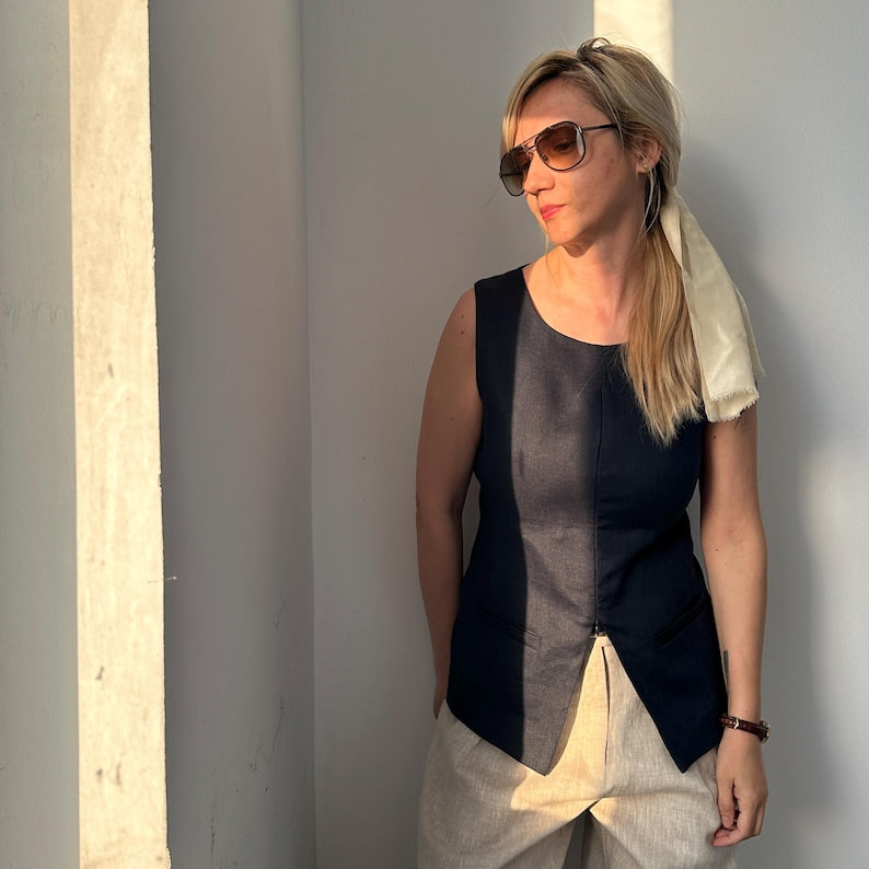 Woman wearing a navy sleeveless top with beige pants against a gray wall.