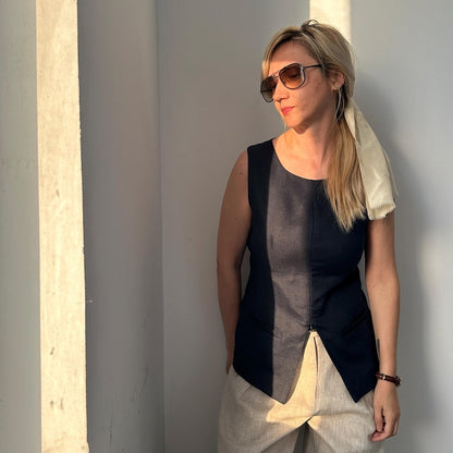 Woman wearing a navy sleeveless top with beige pants against a gray wall.