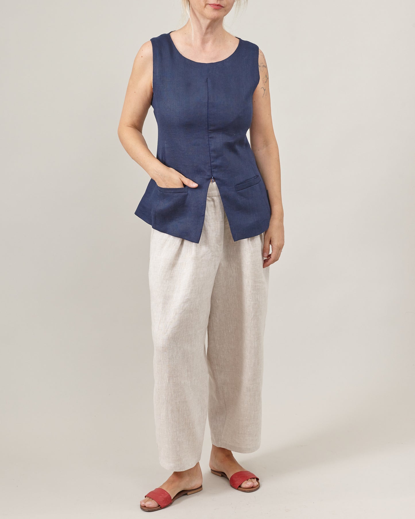 Woman wearing a navy sleeveless top and beige pants on a plain background