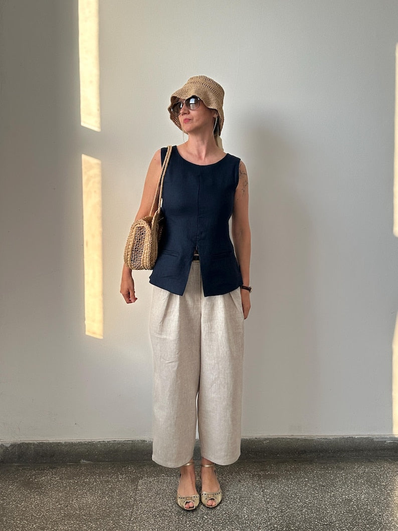 Woman wearing a navy sleeveless top and beige wide-leg pants, standing against a plain wall.