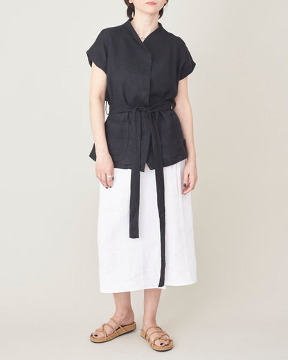 Person wearing a black top and white pants with a belt on a plain background