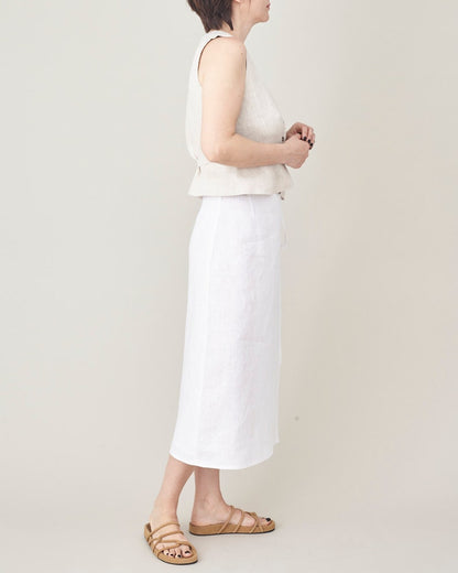 Person wearing a white sleeveless top and skirt with beige sandals on a plain background