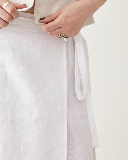 Close-up of a person adjusting a white tie waist skirt with a neutral background