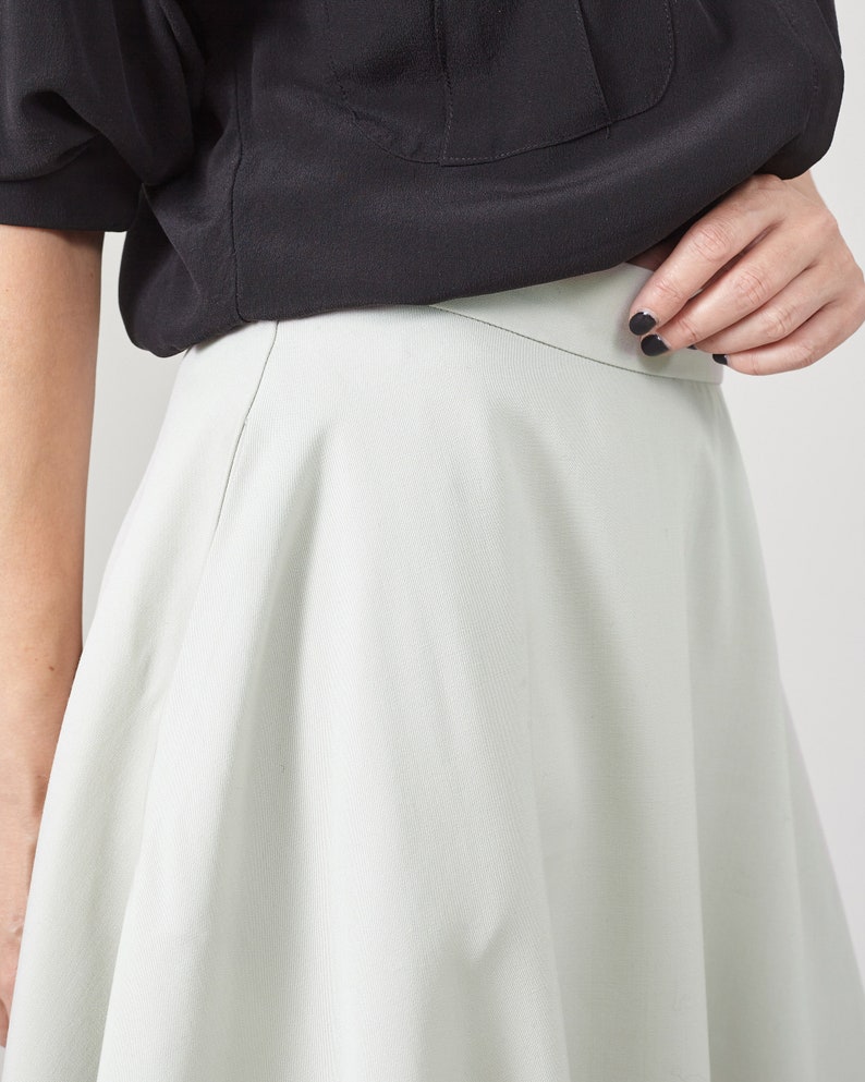 Person wearing a black top and light mint skirt on a plain background