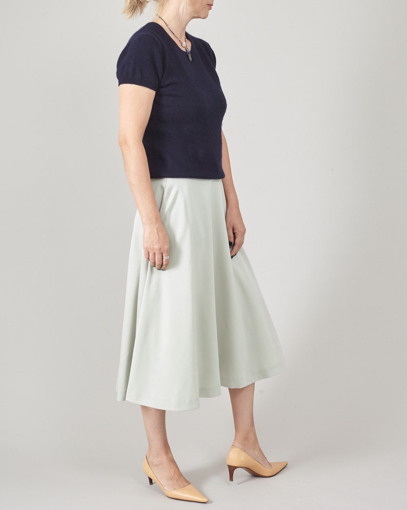 Woman wearing a navy top and light mint skirt on a plain background