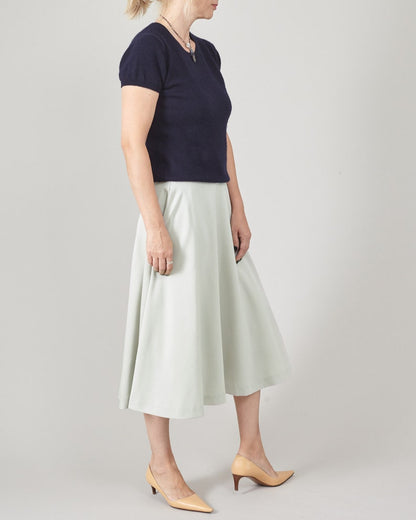 Woman wearing a navy top and light mint skirt on a plain background