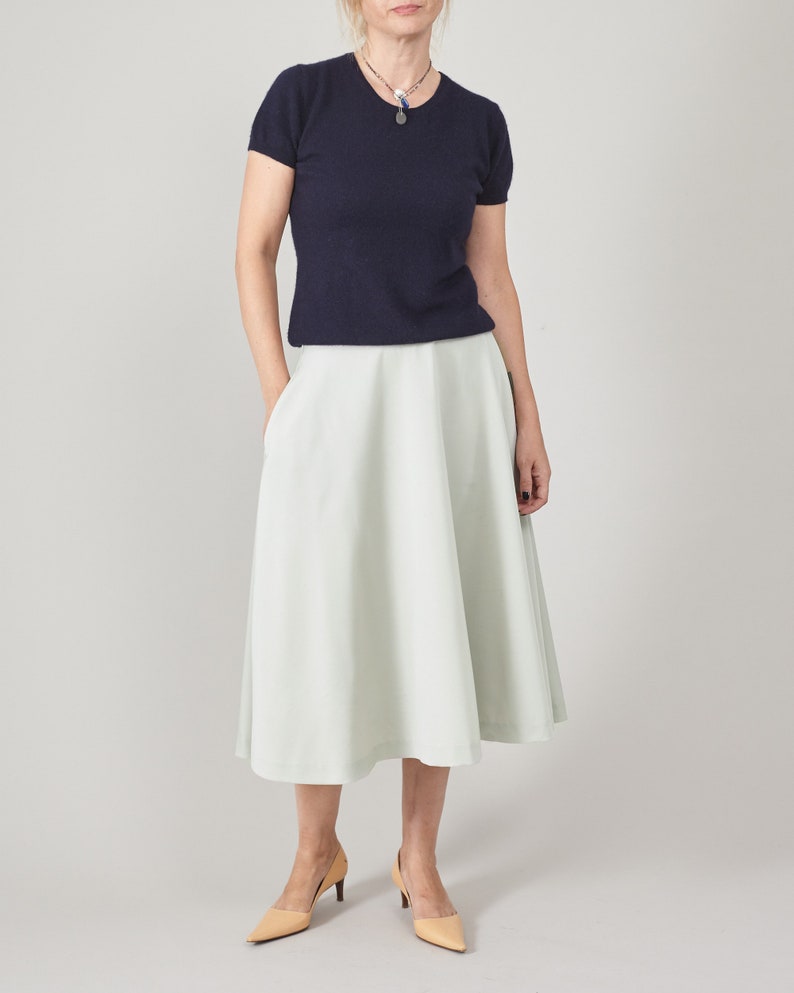 Woman wearing a navy top and mint skirt on a plain background
