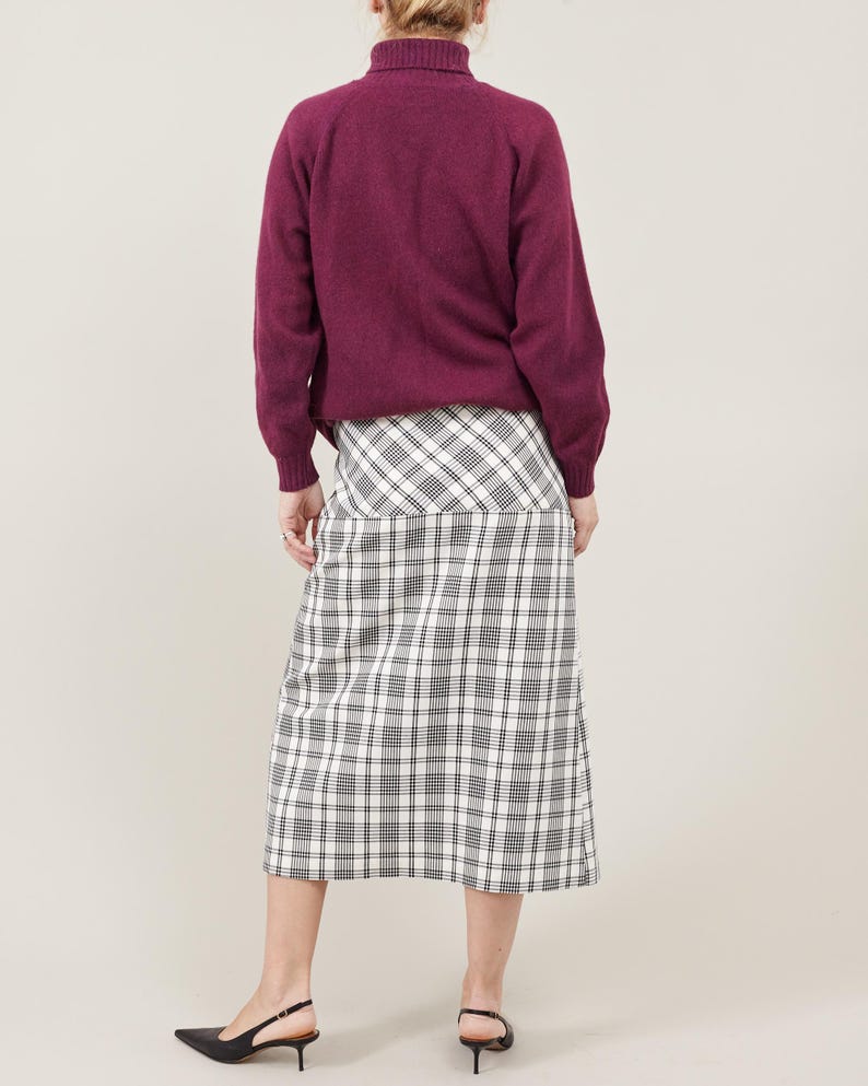Person wearing a purple sweater and plaid skirt on a plain background