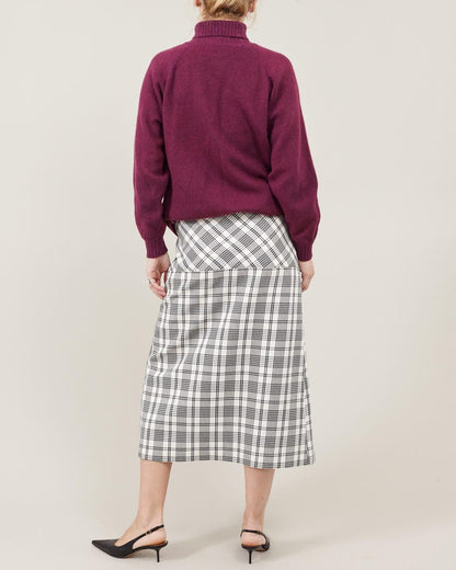 Person wearing a purple sweater and plaid skirt on a plain background