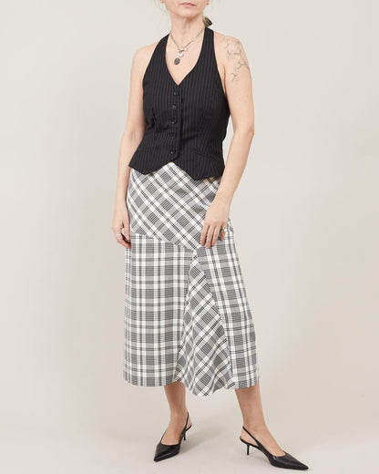 Person wearing a black sleeveless top and plaid skirt on a plain background