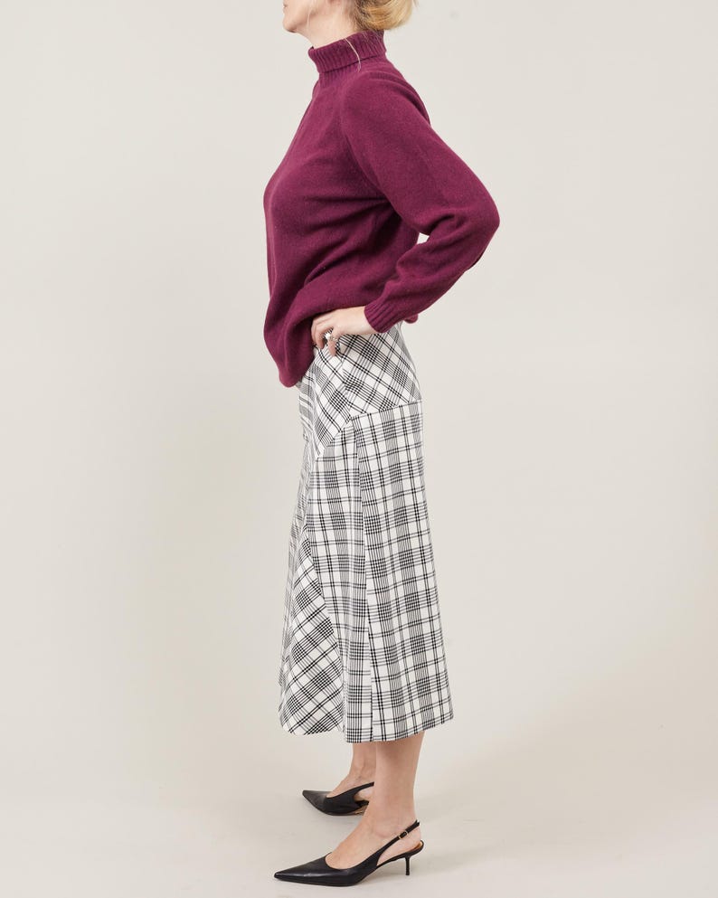 Person wearing a purple sweater and plaid midi skirt on a plain background