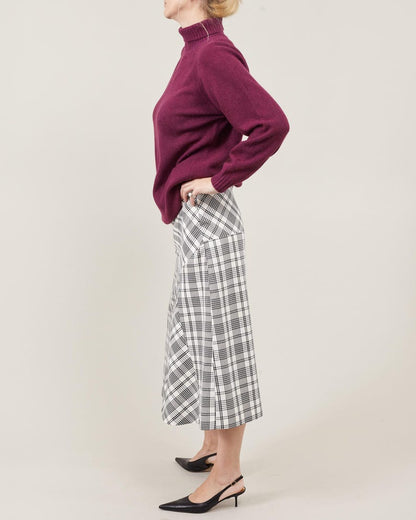 Person wearing a purple sweater and plaid midi skirt on a plain background