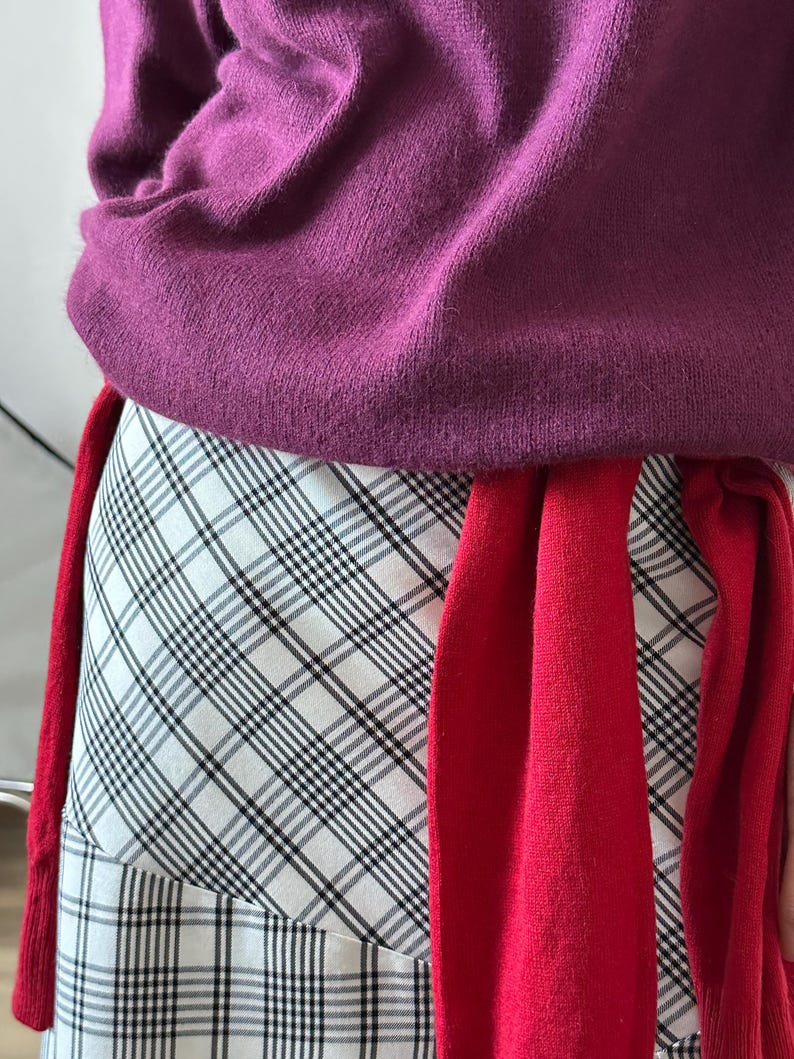 Person wearing a purple sweater and red scarf with plaid patterned skirt.
