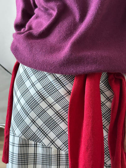 Person wearing a purple sweater and red scarf with plaid patterned skirt.