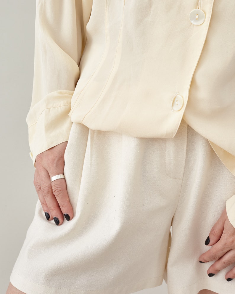 Close-up of high-waisted raw silk Bermuda shorts featuring elegant pleats, paired with a matching natural silk top