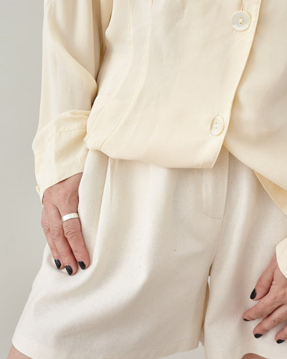 Close-up of high-waisted raw silk Bermuda shorts featuring elegant pleats, paired with a matching natural silk top
