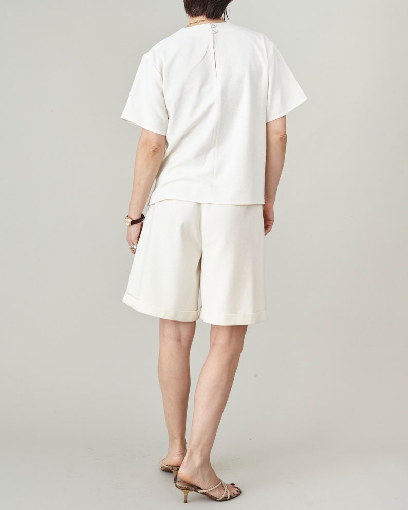 Person wearing a white outfit with shorts on a plain background
