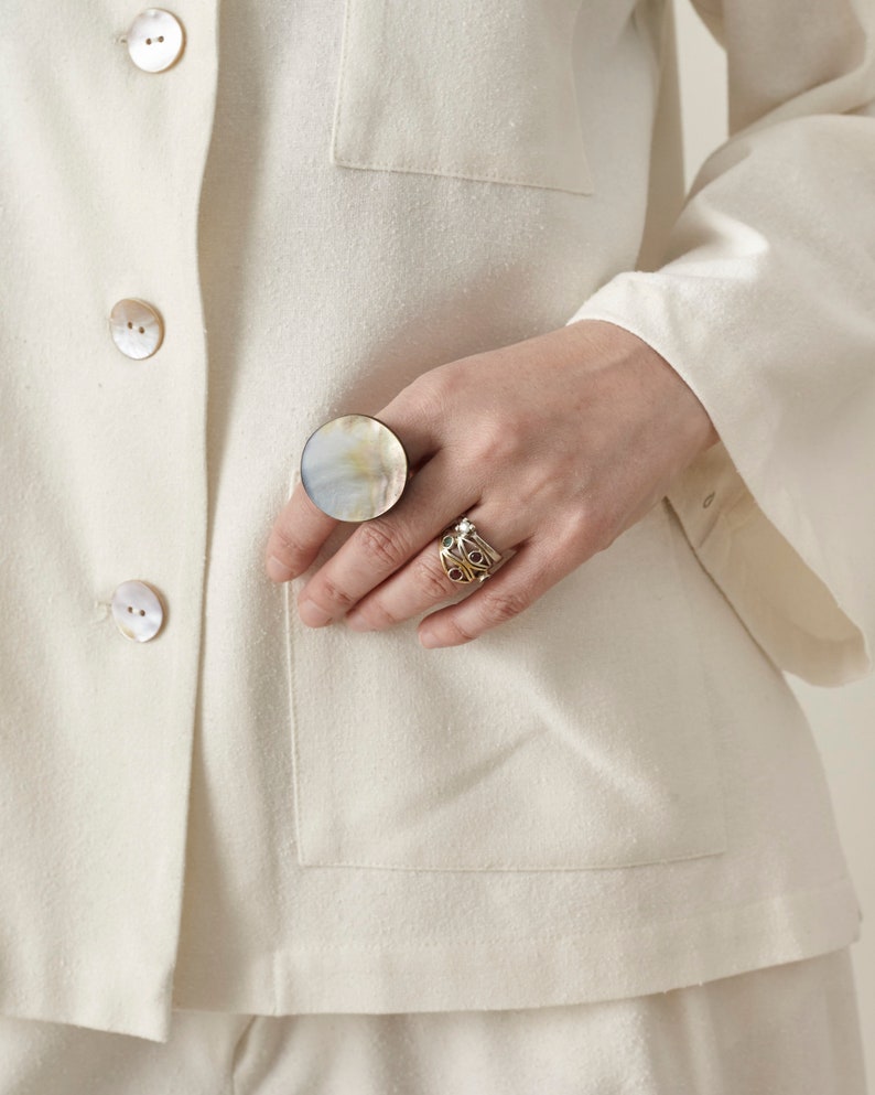 Close-up of a person wearing an offwhite blouse with a ring on a neutral background