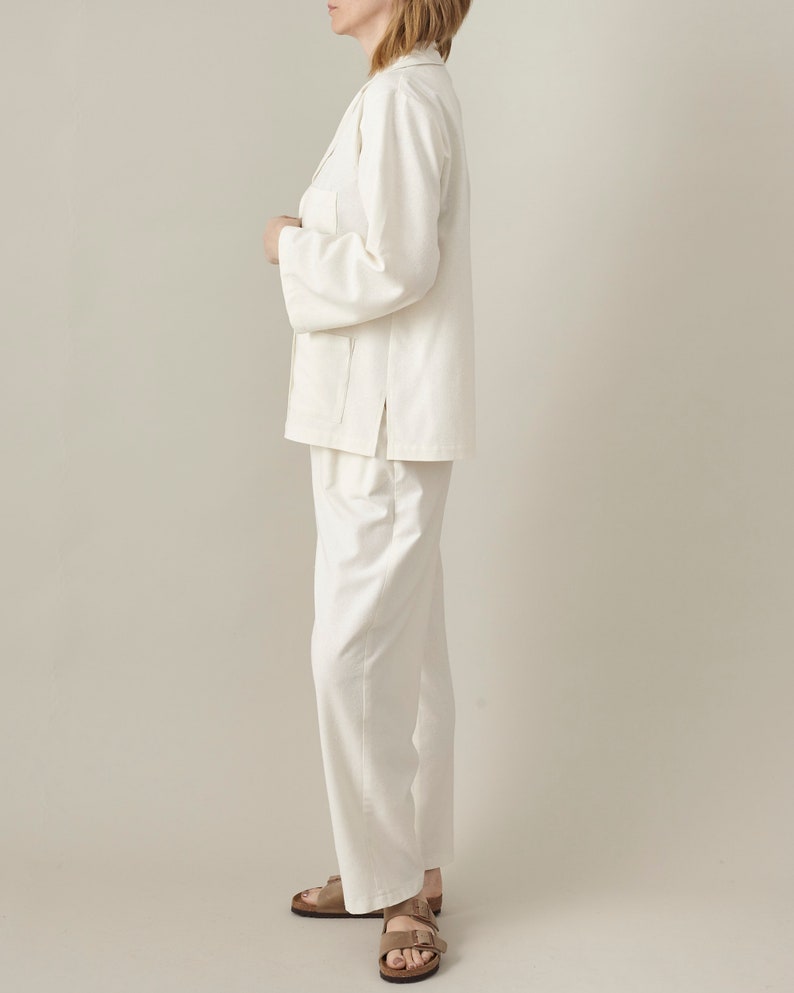 Person wearing a white suit standing against a plain background