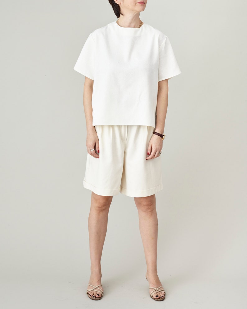 Person wearing a white top and beige skirt on a plain background