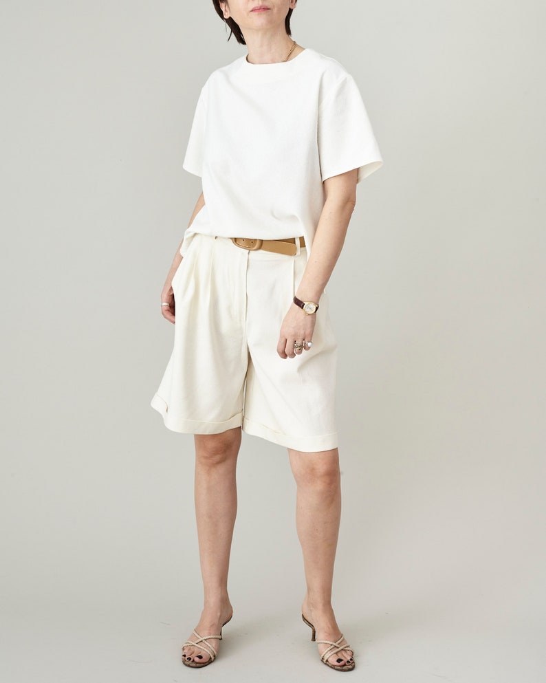 Person wearing an off white t-shirt and matching bermuda shorts on a plain background