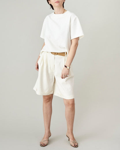 Person wearing an off white t-shirt and matching bermuda shorts on a plain background