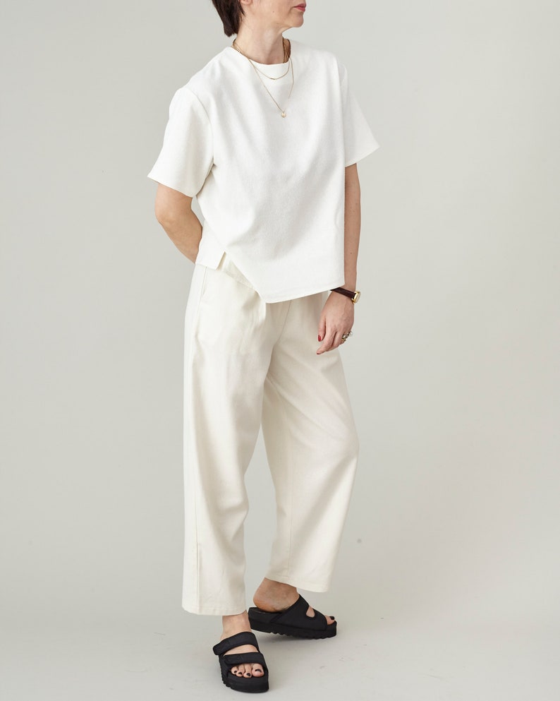 Person wearing a white top and matching tapered pants on a plain background