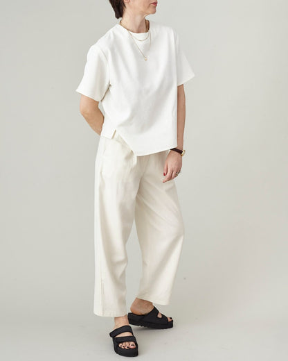 Person wearing a white top and matching tapered pants on a plain background