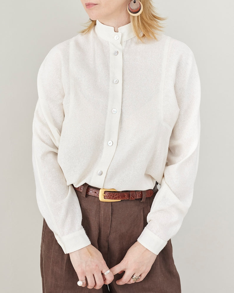 Person wearing a white  raw silk button-up mandarin collar shirt and brown pants on a plain background