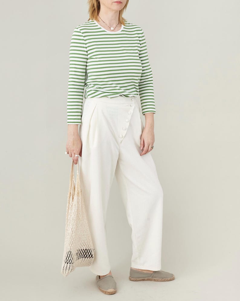 Person wearing a green and white striped shirt with white pants, holding a net bag on a plain background