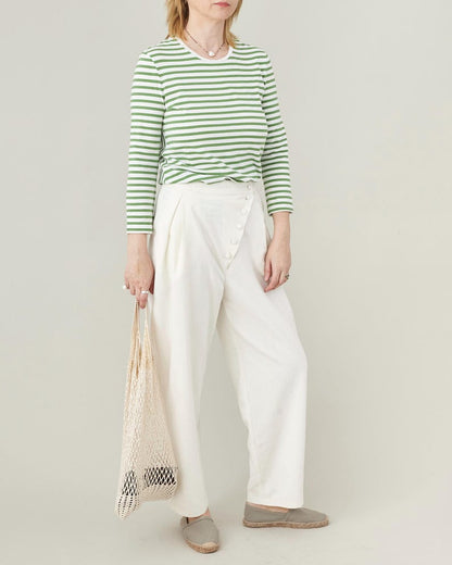 Person wearing a green and white striped shirt with white pants, holding a net bag on a plain background
