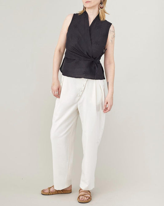 Person wearing a black sleeveless top and white pants on a plain background