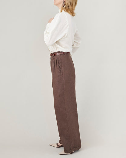Person wearing a white blouse and brown wide-leg pants on a plain background