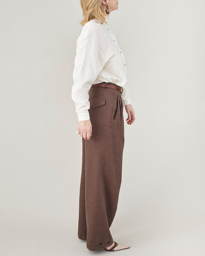 Person wearing a white shirt and brown wide-leg pants on a plain background