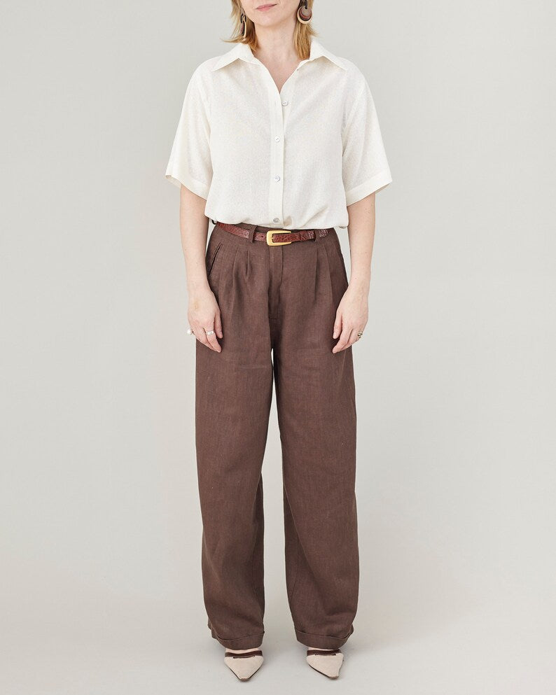 Person wearing a white short sleeve oversized shirt and brown linen pants on a plain background