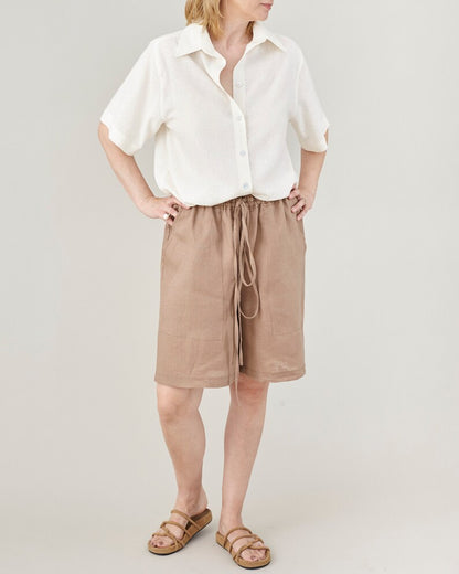 Person wearing a white shirt and brown shorts on a plain background